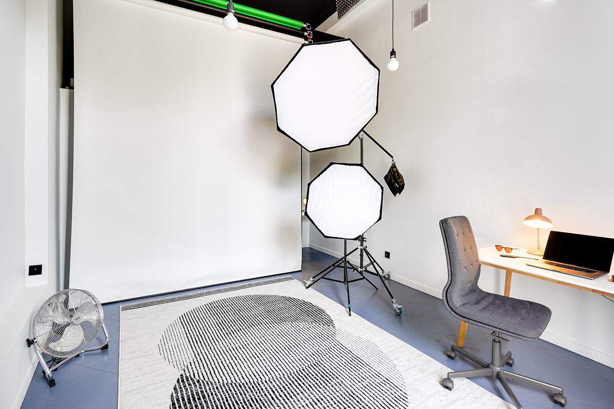 Zdjęcie wnętrz studia fotograficznego Marka Wołynko w Warszawie na ulicy Miedziana 10. Na zdjęciu widać tła fotograficzne, profesjonalny sprzęt fotografizny, lampy, statywy, wentylator. Po prawej stronie biurka i krzesło.