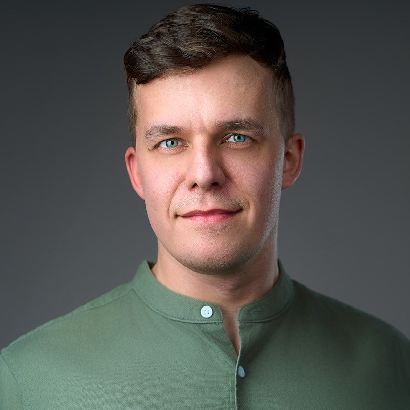 Męski portret typu headshot na szarym tle.